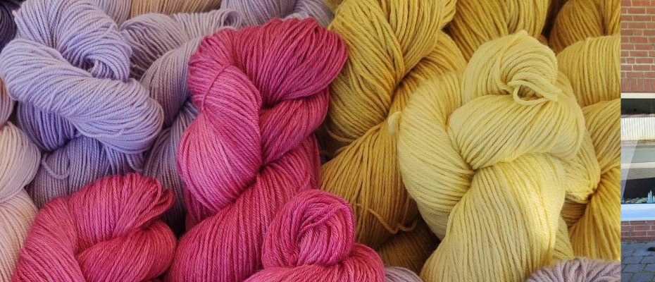 Bunte Garnknäuel in Rosa-, Beige-, Violett- und Gelbtönen vor einem Laden mit Schaufenereinrichtung.